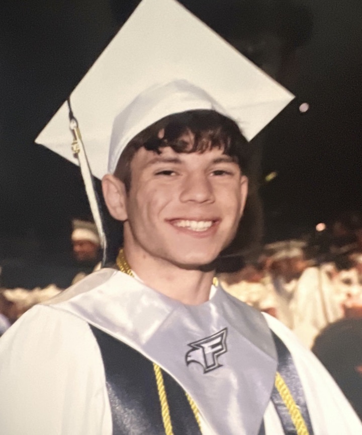 David Cabrera smiling in a white graduation cap and gown